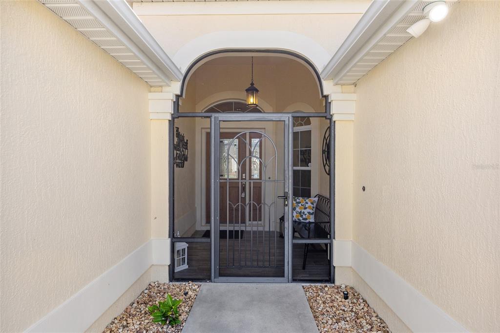 A covered entryway features a screened-in porch, a decorative metal door, and a concrete walkway — 1440 ALESIO STREET, THE VILLAGES, FL