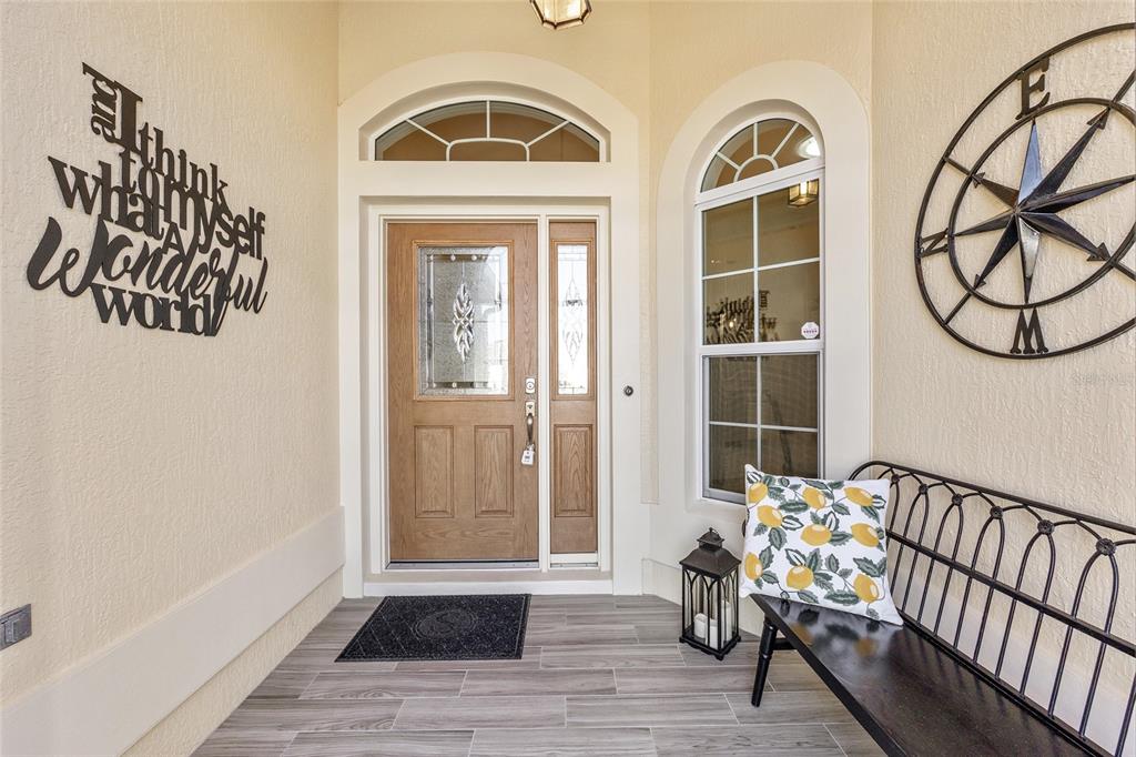 A front porch features a wooden door with glass panels, a bench, and wall decor — 1440 ALESIO STREET, THE VILLAGES, FL