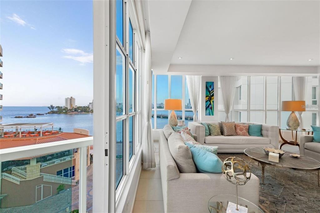 A bright living room with floor-to-ceiling windows overlooking the ocean and a coastal city — 25 MUÑOZ RIVERA AVE UNIT 614, SAN JUAN, PR
