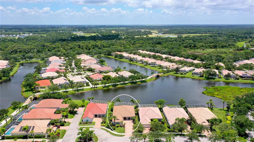 An aerial view shows a tan house with a pool cage beside a lake — 8672 DOLCE LANE, SARASOTA, FL
