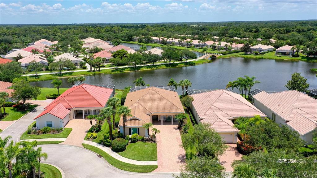 An aerial view shows several suburban houses with tiled roofs situated along a lake — 8672 DOLCE LANE, SARASOTA, FL