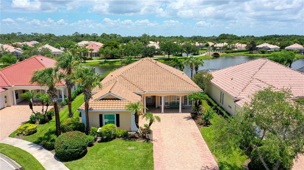 An aerial view shows a tan house with a tiled roof and brick paver driveway — 8672 DOLCE LANE, SARASOTA, FL