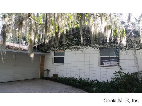 A white concrete block house features a garage and windows covered in climbing ivy — 908 SE 23 STREET, OCALA, FL