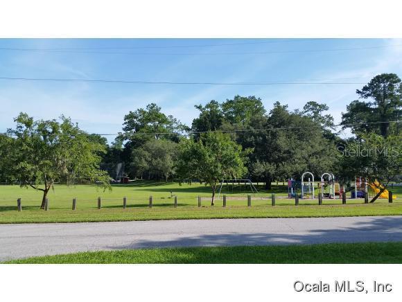 A grassy park features a playground, trees, and a wooden fence along a paved road — 908 SE 23 STREET, OCALA, FL