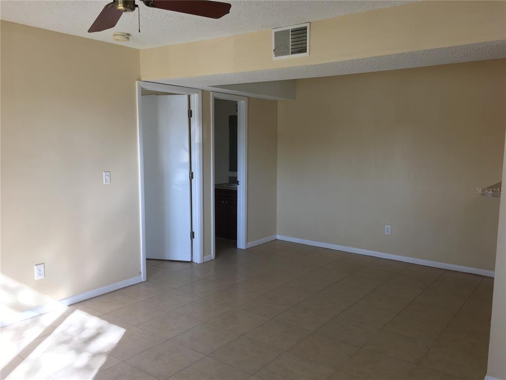 A room with beige walls, tile flooring, a ceiling fan, and two doorways — 455 ALT 19 S UNIT 141, PALM HARBOR, FL