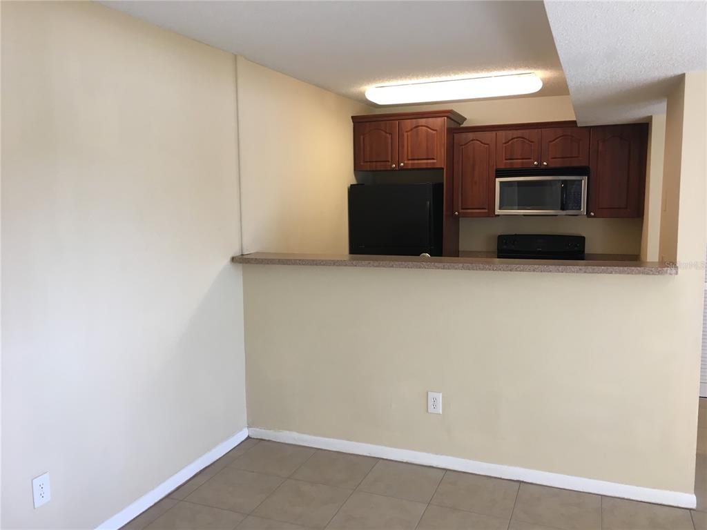 A kitchen with dark wood cabinets, black appliances, and a breakfast bar overlooking a room — 455 ALT 19 S UNIT 141, PALM HARBOR, FL