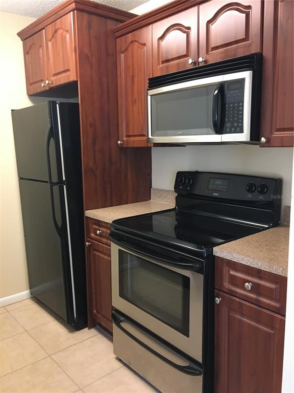 A kitchen features dark wood cabinets, a black refrigerator, and a stainless steel oven — 455 ALT 19 S UNIT 141, PALM HARBOR, FL