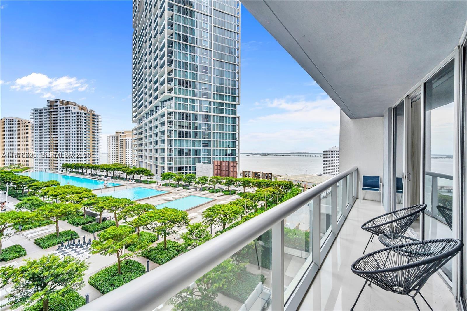 A balcony with two chairs overlooks a swimming pool, landscaped courtyard, and a high-rise building — 485 Brickell Ave # 1711, Miami FL 33131, MIAMI, FL