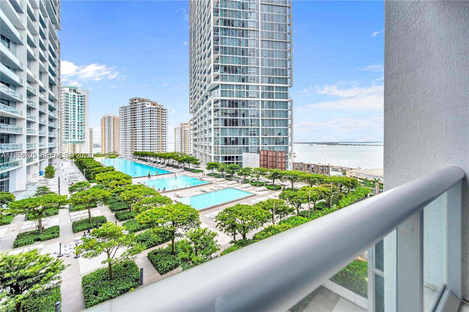 A balcony view overlooks a landscaped pool deck between high-rise residential buildings near the water — 485 Brickell Ave # 1711, Miami FL 33131, MIAMI, FL