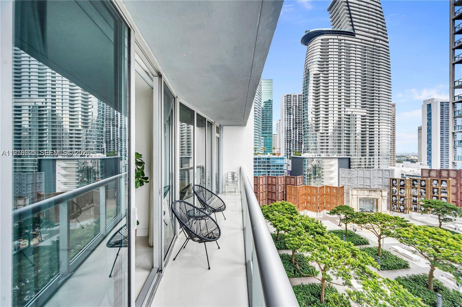 A balcony with two black chairs overlooks a modern city park and surrounding skyscrapers — 485 Brickell Ave # 1711, Miami FL 33131, MIAMI, FL