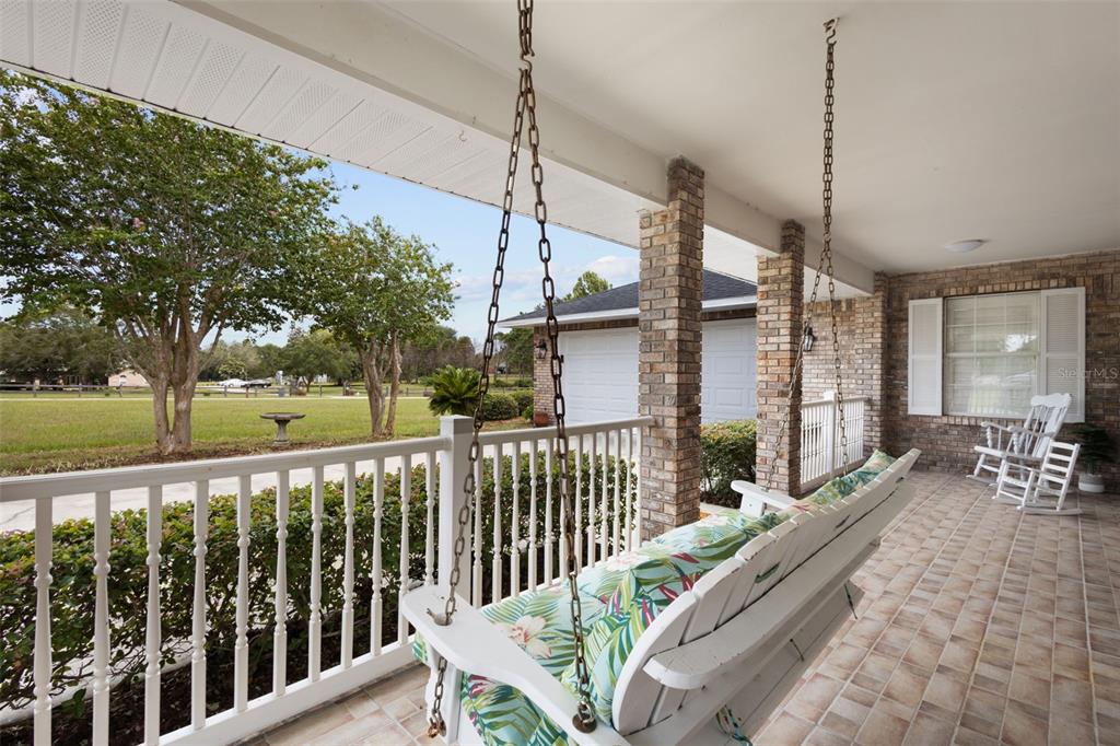A covered porch features a hanging swing, a white railing, and a rocking chair — 8140 MEADOWLARK CT, MELROSE, FL