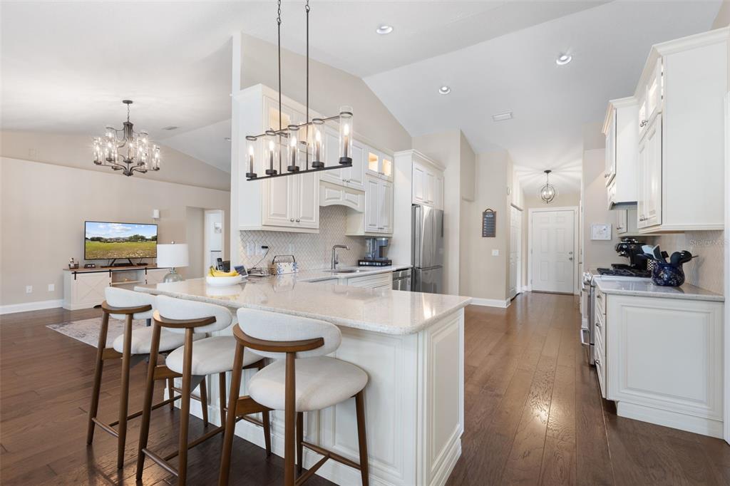 A kitchen with white cabinets, a granite island, and bar stools, opening to a living area — 8140 MEADOWLARK CT, MELROSE, FL