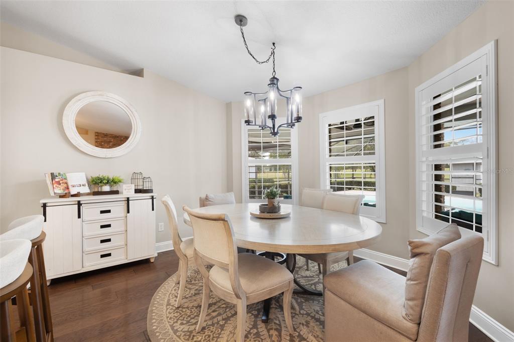 A dining room features a round table, upholstered chairs, a chandelier, and white plantation shutters — 8140 MEADOWLARK CT, MELROSE, FL