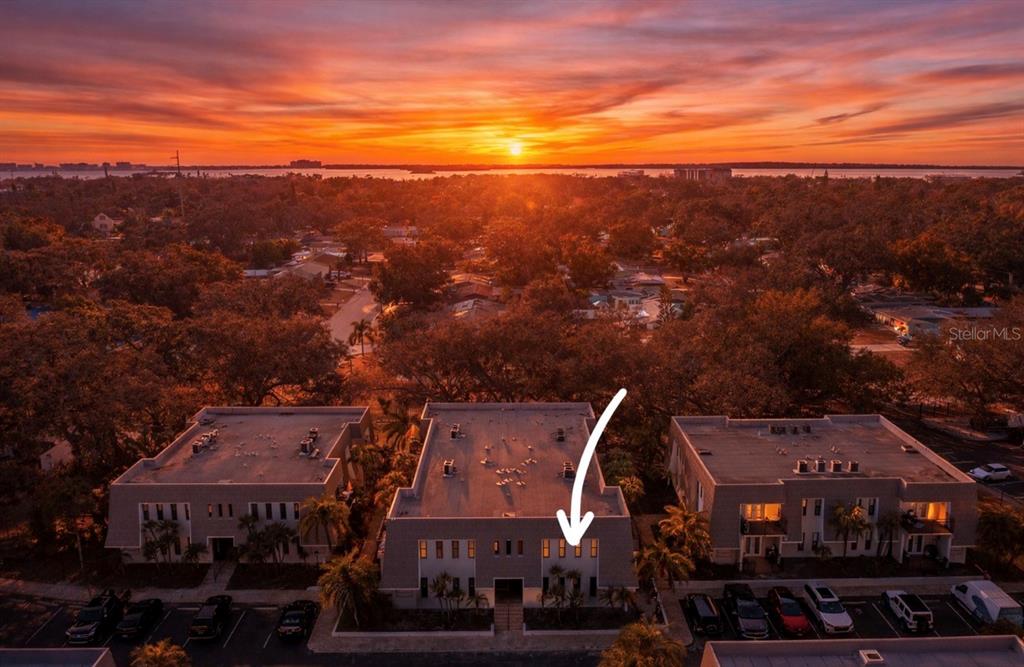 An aerial view shows three multi-story apartment buildings at sunset with an arrow pointing down — 704 LYNDHURST STREET UNIT 624, DUNEDIN, FL