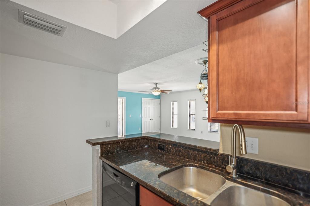 A kitchen with dark granite countertops and a stainless steel sink overlooks a living area — 704 LYNDHURST STREET UNIT 624, DUNEDIN, FL