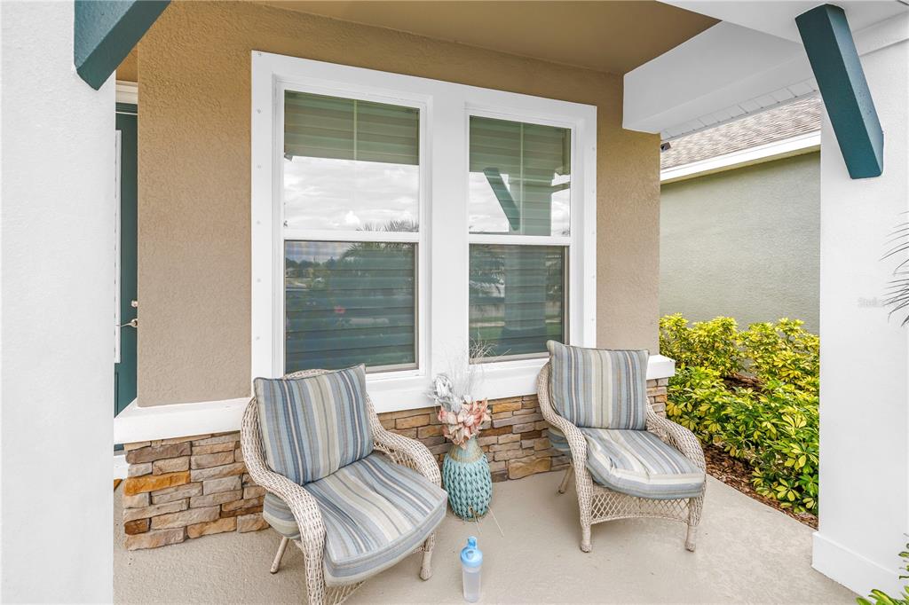 A covered porch features two wicker chairs with striped cushions and a stone-accented wall — 8217 TRIMBELLE, PARRISH, FL