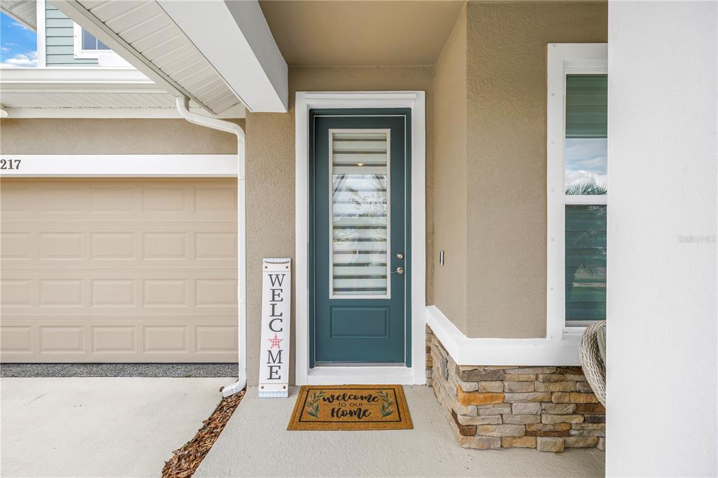 The exterior entrance features a teal front door, a welcome sign, and stone siding — 8217 TRIMBELLE, PARRISH, FL