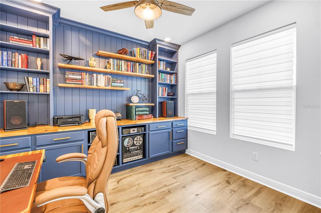 A home office features blue built-in cabinetry, open shelving, a wooden desk, and wood flooring — 8217 TRIMBELLE, PARRISH, FL