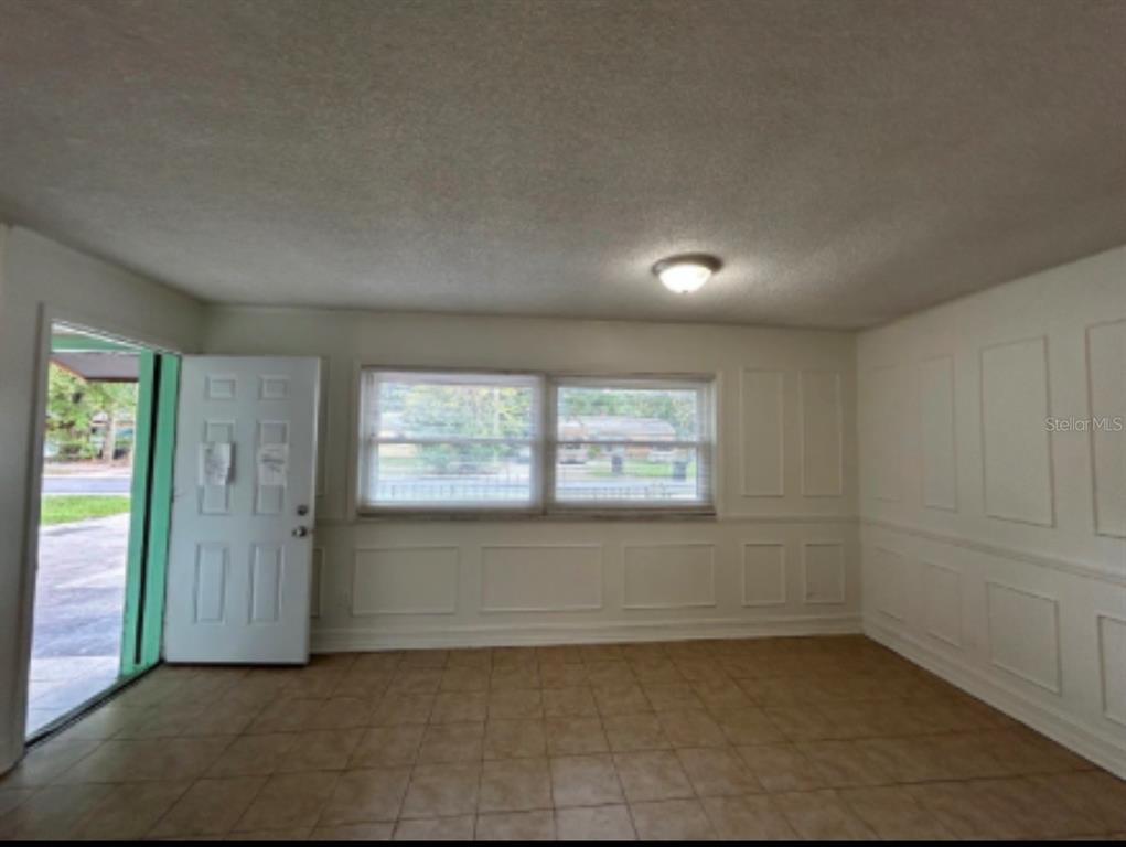 An empty room features tan tile flooring, white wainscoting, and a window overlooking the outdoors — 625 19TH STREET, ORLANDO, FL