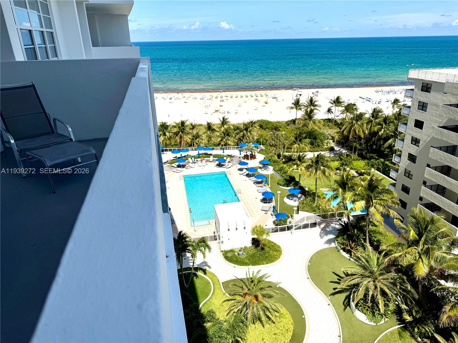 An elevated balcony view overlooks a swimming pool, palm trees, and a sandy beach — 100 Lincoln Rd # 1230, Miami Beach FL 33139, MIAMI BEACH, FL
