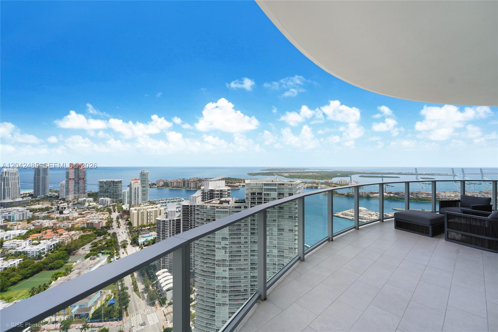 A high-rise balcony with glass railings overlooks a city skyline, harbor, and the ocean — 500 Alton Rd # 4401, Miami Beach FL 33139, MIAMI BEACH, FL