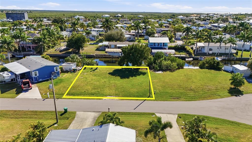 An aerial view shows a vacant, rectangular grassy lot outlined in yellow near a canal — 751 CORAL DRIVE, PUNTA GORDA, FL