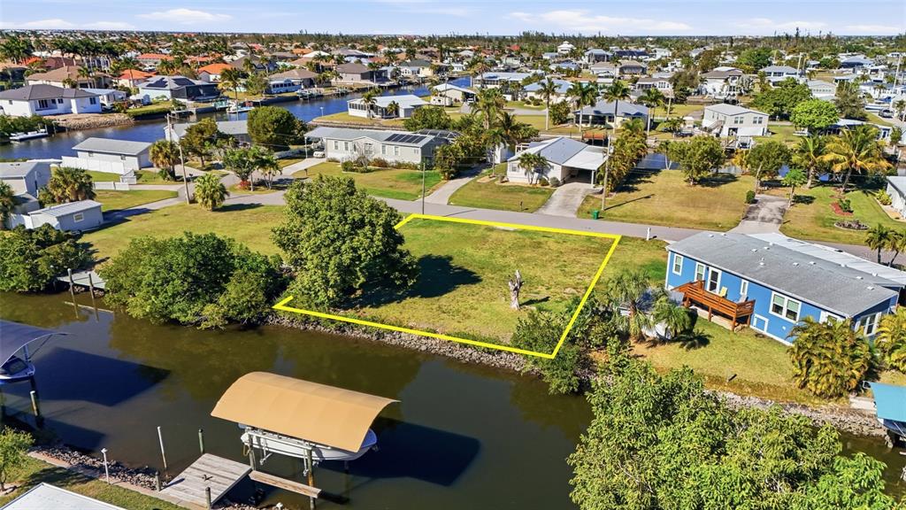 An aerial view shows a vacant waterfront lot outlined in yellow next to a blue house — 751 CORAL DRIVE, PUNTA GORDA, FL