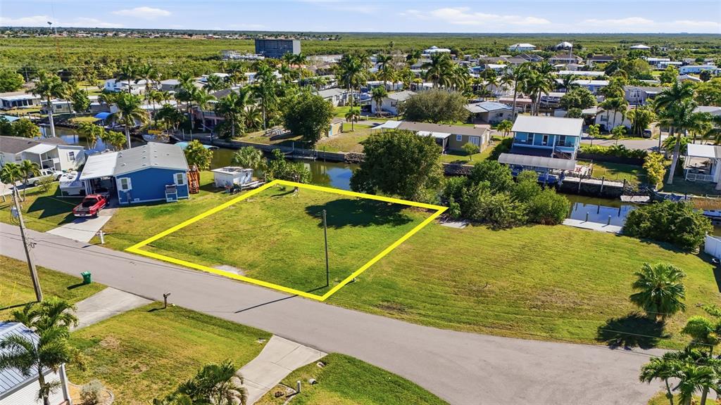 An aerial view shows a vacant, rectangular grassy lot outlined in yellow next to a canal — 751 CORAL DRIVE, PUNTA GORDA, FL