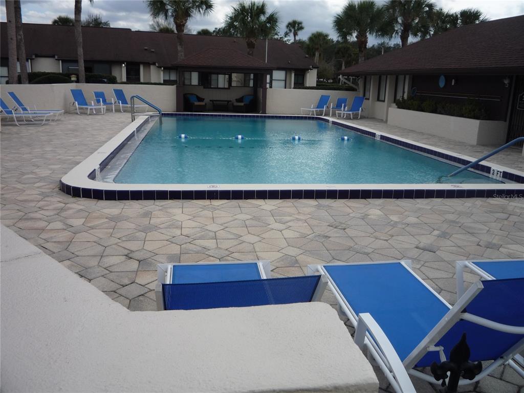 A rectangular swimming pool is surrounded by a paved deck with blue lounge chairs — 101 GRAND PLAZA DRIVE UNIT F3, ORANGE CITY, FL