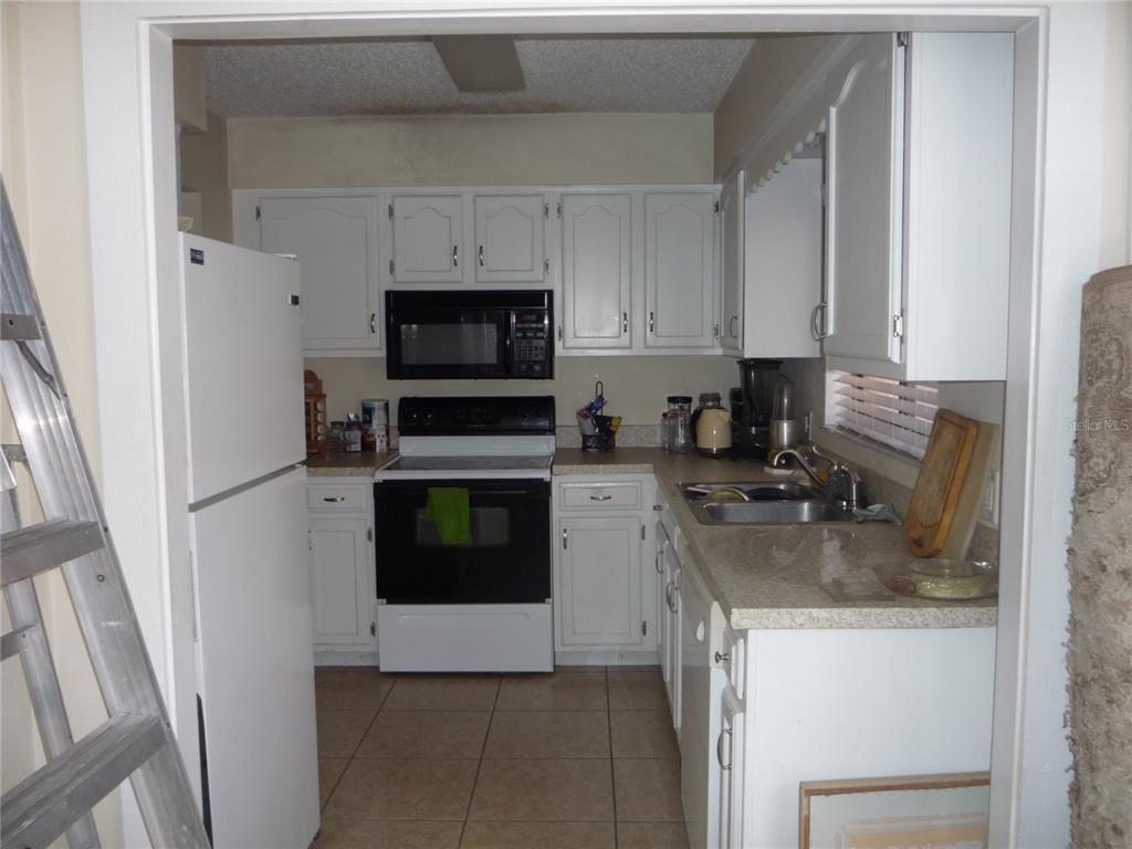 A kitchen features white cabinets, a black stove and microwave, and light-colored countertops — 101 GRAND PLAZA DRIVE UNIT F3, ORANGE CITY, FL