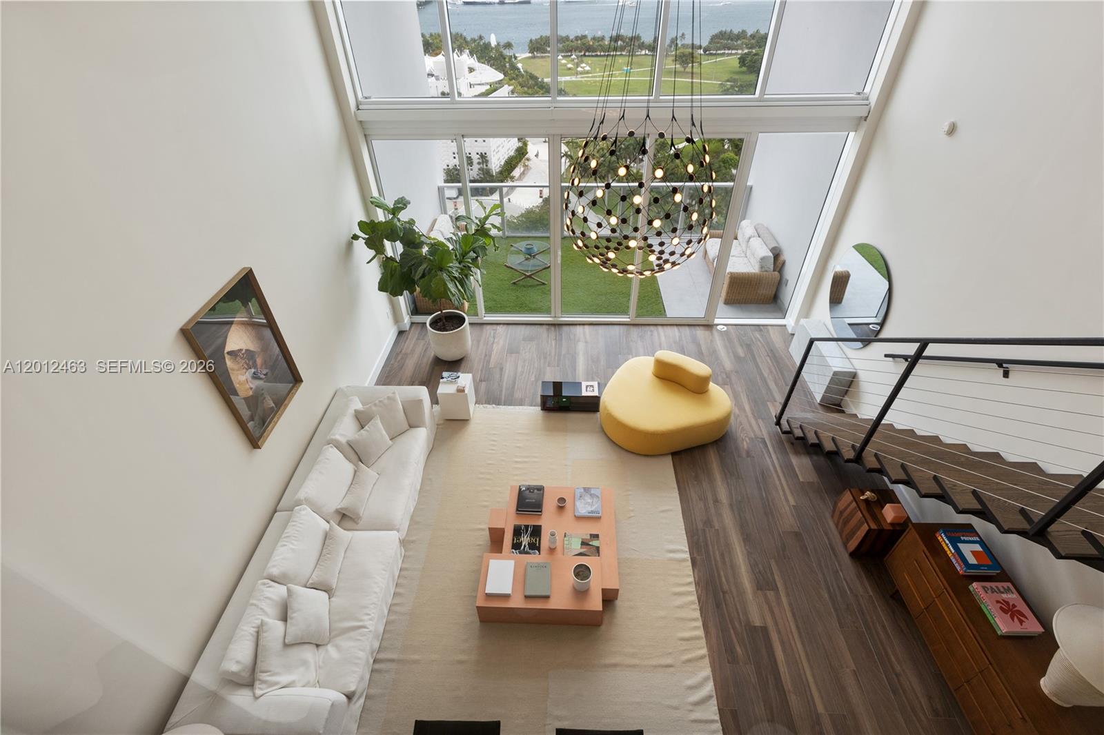 A high-ceilinged living room features a white sofa, yellow lounge chair, and large glass windows — 1040 Biscayne Blvd # 1602, Miami FL 33132, MIAMI, FL