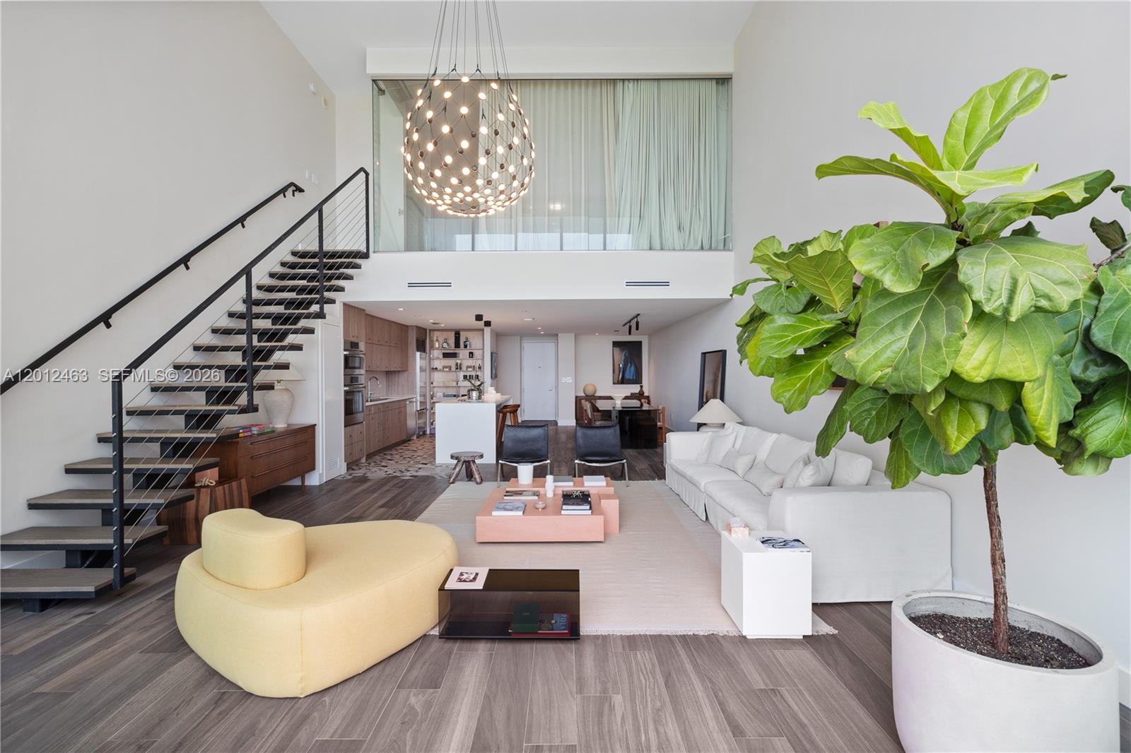 A modern living room features a floating staircase, a large chandelier, and a fiddle-leaf fig — 1040 Biscayne Blvd # 1602, Miami FL 33132, MIAMI, FL