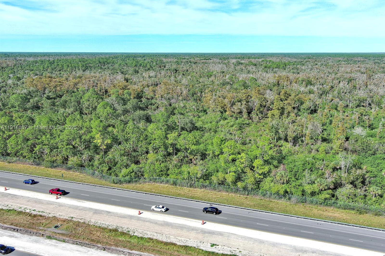 An aerial view shows a multi-lane highway running alongside a large, dense forest area — 0 Alligator Alley, Naples FL 34117, NAPLES, FL