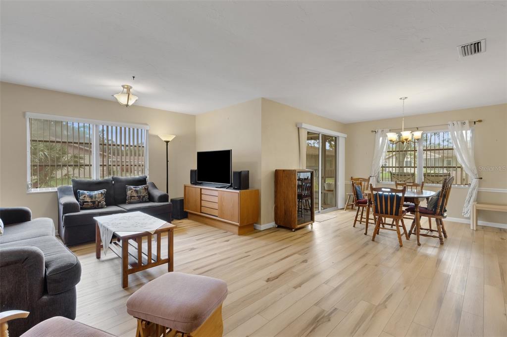A living and dining area with light wood flooring, a television console, and sliding glass doors — 4574 MOHICAN UNIT 151, SARASOTA, FL