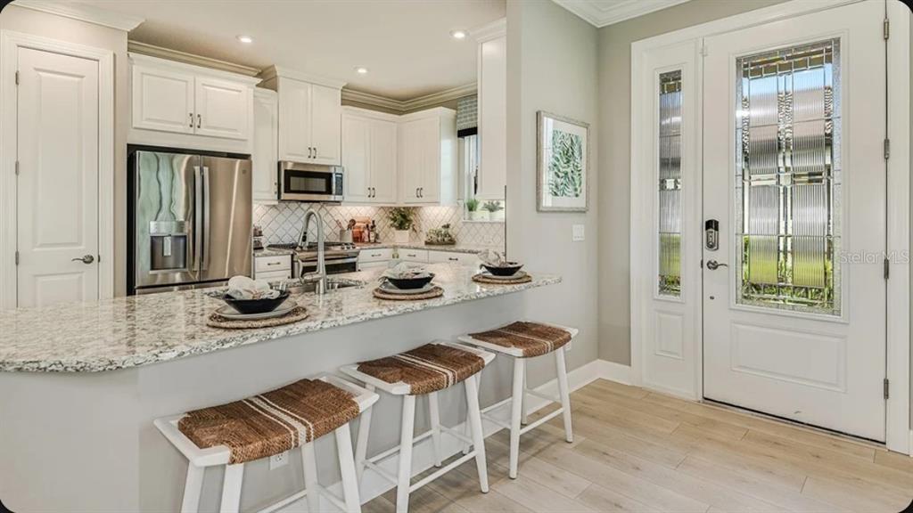A kitchen with white cabinets, granite countertops, and three bar stools near an entryway door — 14537 DERNA TERRACE, BRADENTON, FL