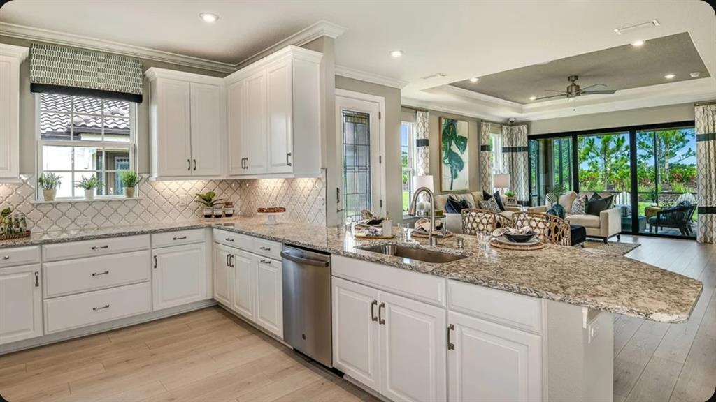 A kitchen with white cabinets, granite countertops, and a stainless steel dishwasher overlooks a living area — 14537 DERNA TERRACE, BRADENTON, FL