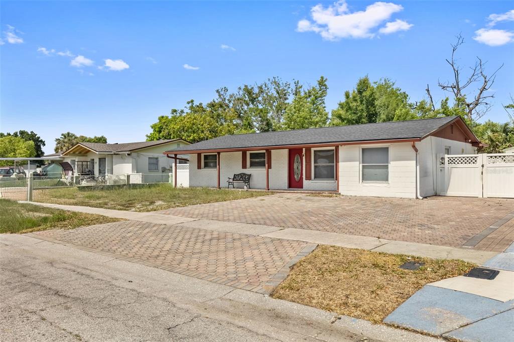 A single-story white house with a red door and a paved driveway under a blue sky — 5923 YORKSHIRE ROAD, TAMPA, FL