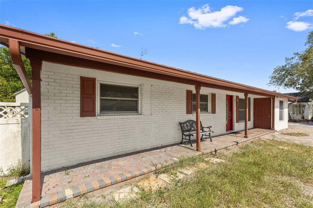 A single-story white brick house features a covered brick patio and a red front door — 5923 YORKSHIRE ROAD, TAMPA, FL