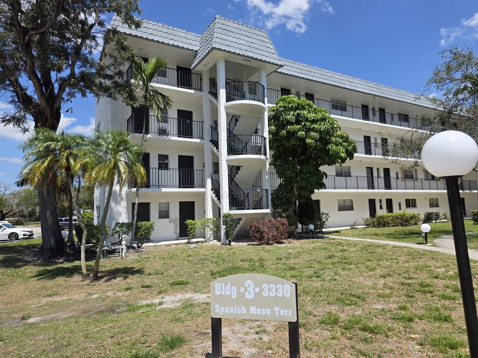 A three-story white apartment building features exterior staircases and a sign in the foreground — 3330 Spanish Moss Terrace # 113, Lauderhill FL 33319, LAUDERHILL, FL