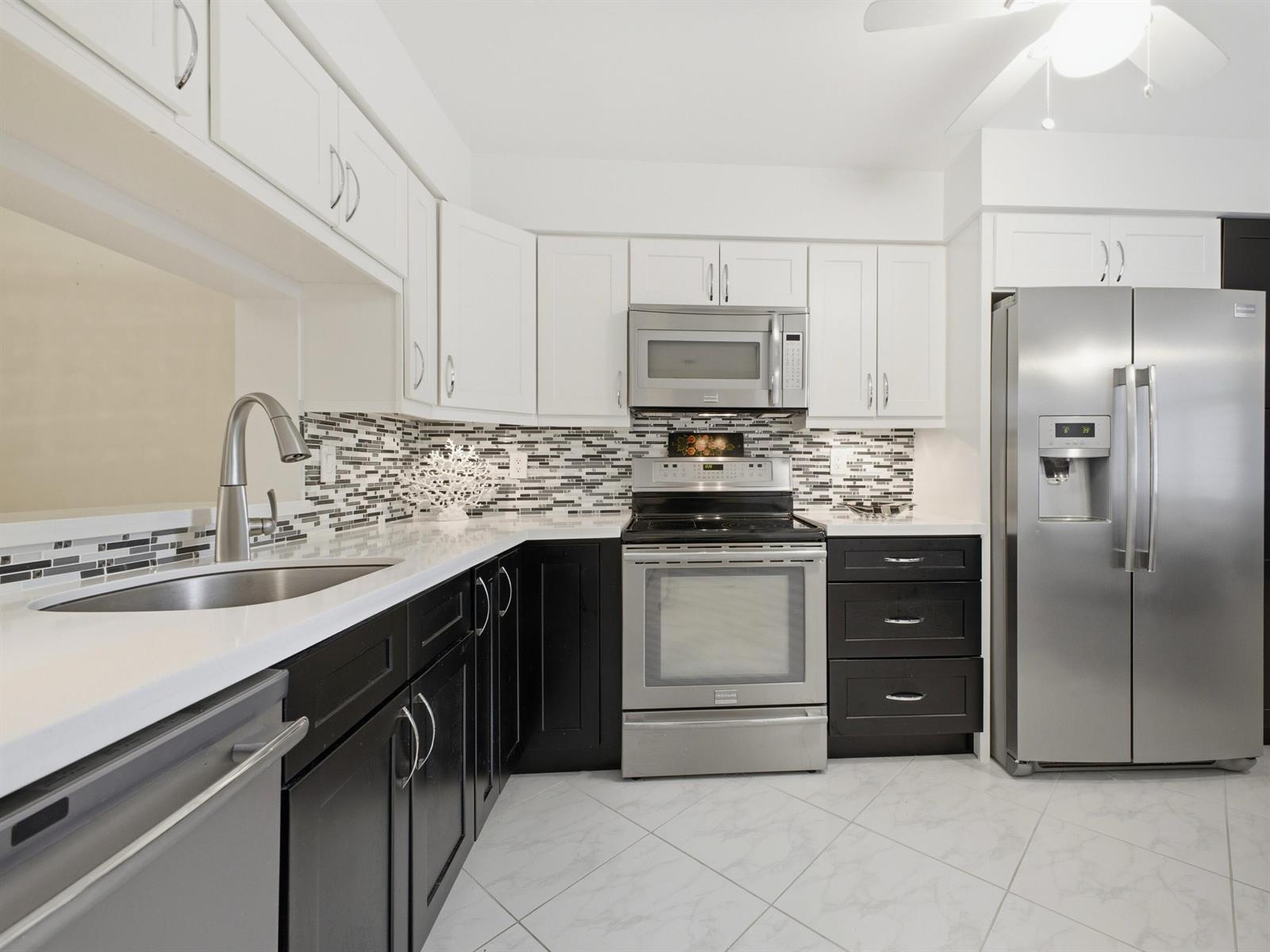 A kitchen with white upper cabinets, black lower cabinets, stainless steel appliances, and tiled backsplash — 7280 Amberly Lane # 201, Delray Beach FL 33446, DELRAY BEACH, FL