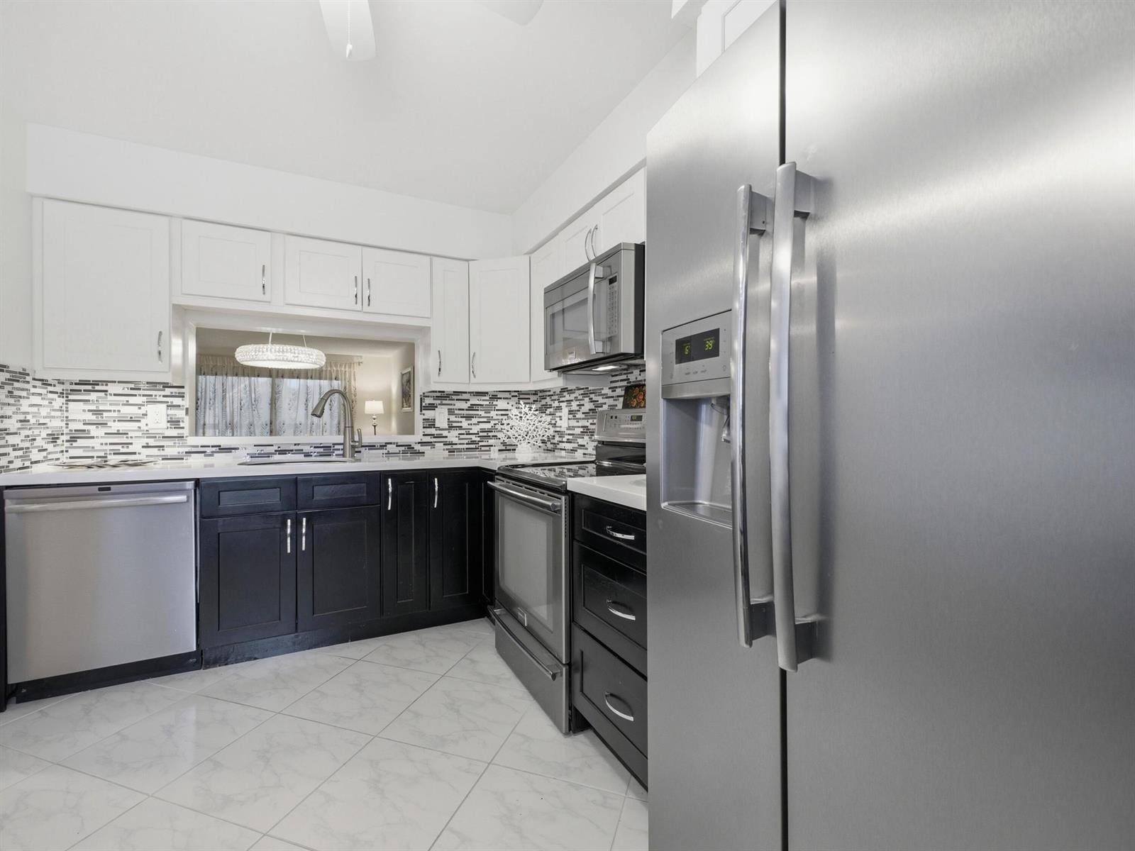A kitchen features white upper cabinets, dark lower cabinets, stainless steel appliances, and tiled floors — 7280 Amberly Lane # 201, Delray Beach FL 33446, DELRAY BEACH, FL