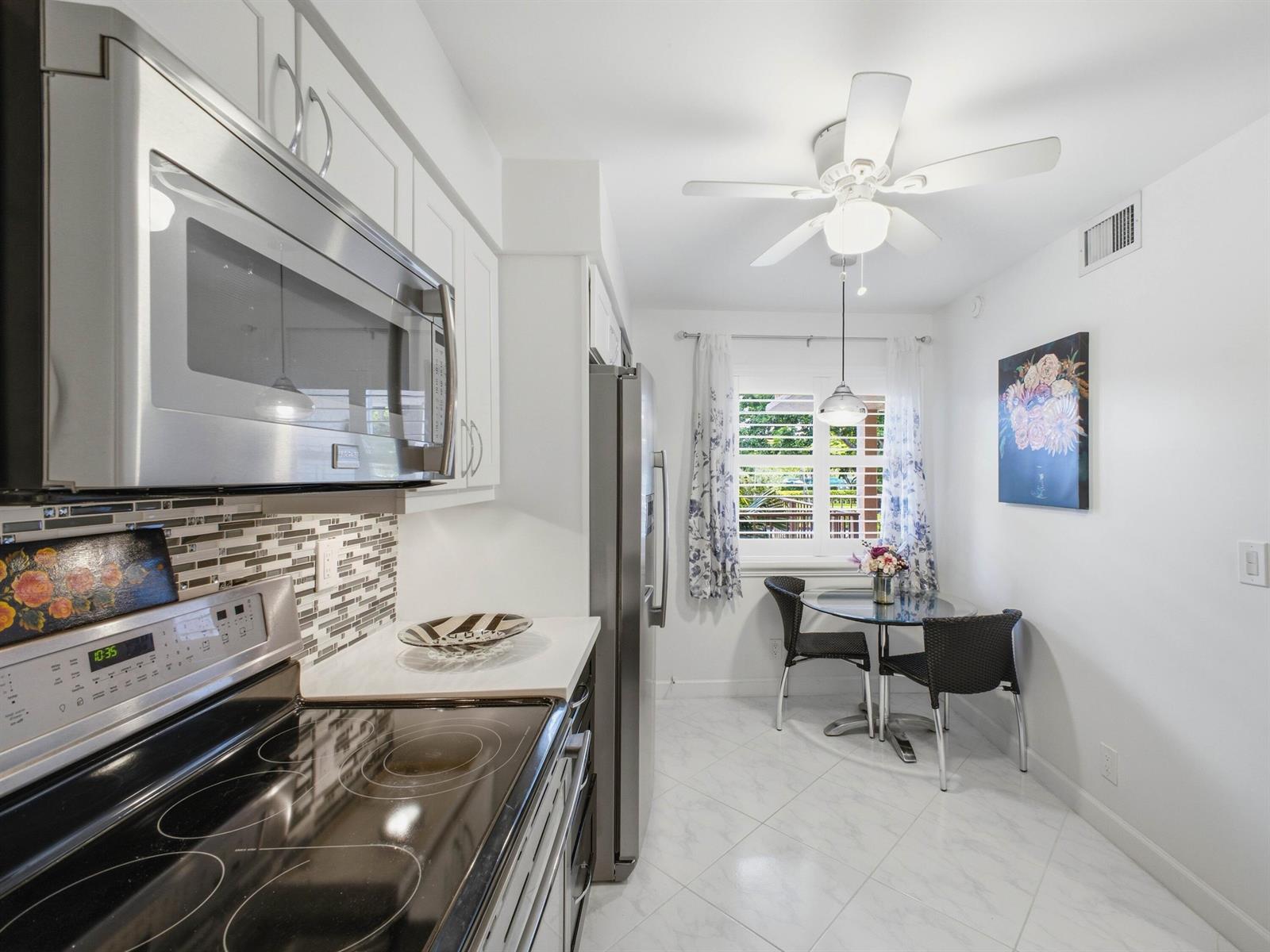 A kitchen with stainless steel appliances, white cabinets, and a small dining area by a window — 7280 Amberly Lane # 201, Delray Beach FL 33446, DELRAY BEACH, FL