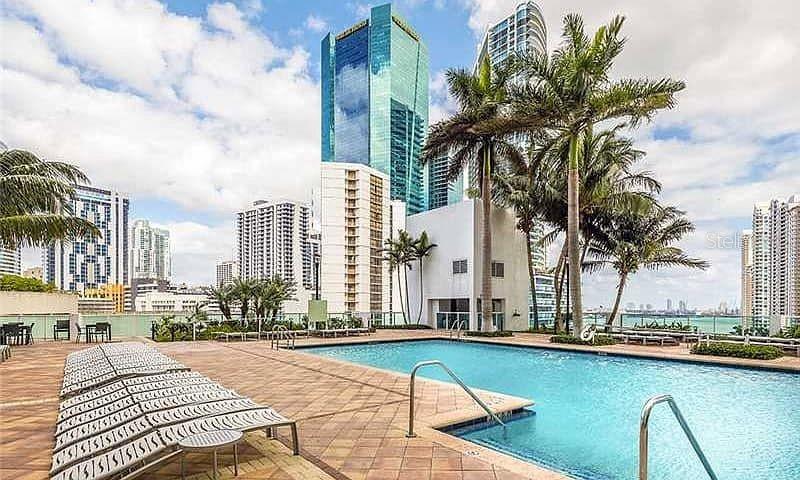 An outdoor swimming pool with lounge chairs on a paved deck surrounded by city skyscrapers — 31 SE 5TH STREET UNIT 305, MIAMI, FL