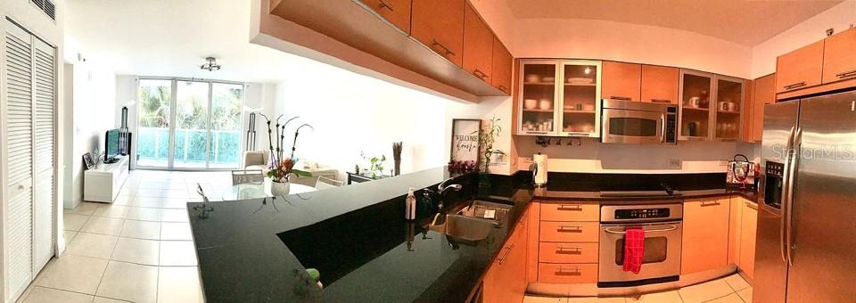 A kitchen with light wood cabinets and black countertops opens into a bright living area — 31 SE 5TH STREET UNIT 305, MIAMI, FL