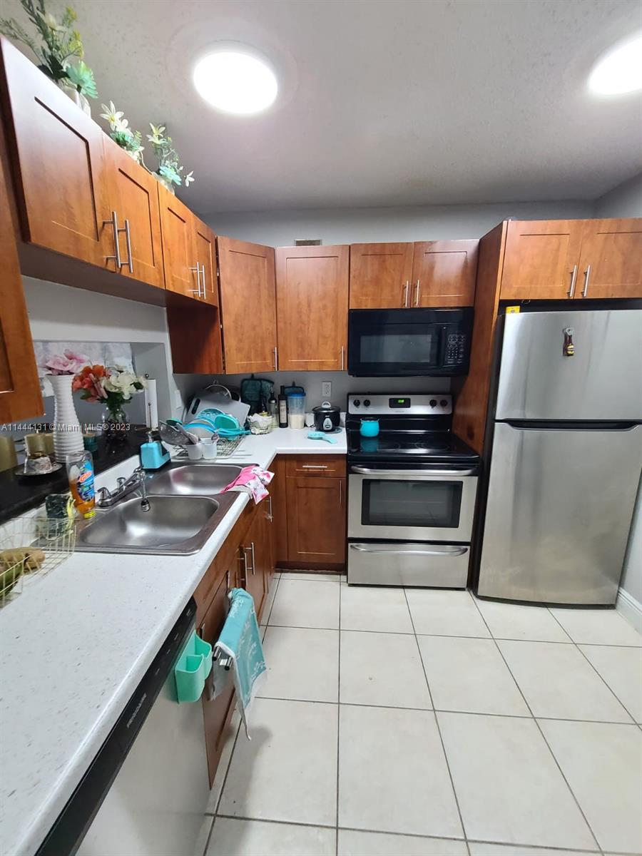 A kitchen features wood cabinets, stainless steel appliances, and white countertops over tiled floors — 496 NW 165th St Rd # D112, Miami FL 33169, MIAMI, FL