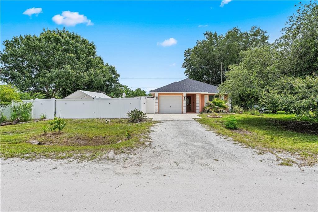 A single-story house with a garage and a white fence sits on a gravel driveway — VERO BEACH, FL