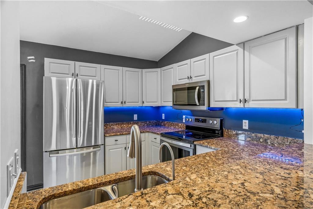 A kitchen features light gray cabinets, granite countertops, stainless steel appliances, and blue under-cabinet lighting — VERO BEACH, FL