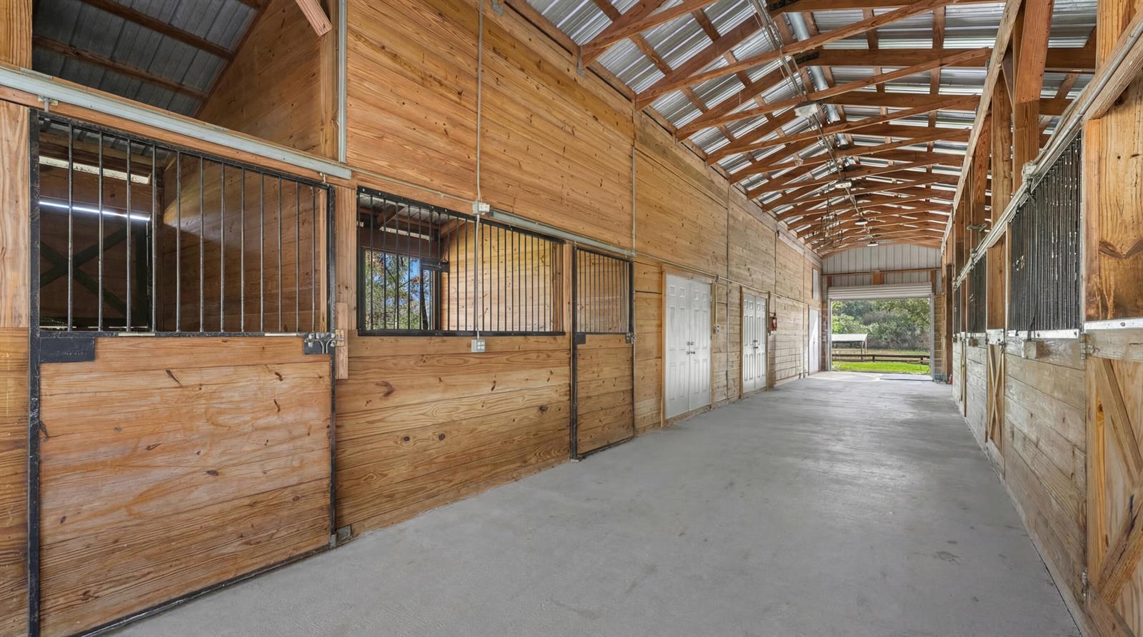 An interior view of a horse barn with wooden stalls, concrete flooring, and exposed rafters — 12440 Tangerine Boulevard, FL 33412, FL