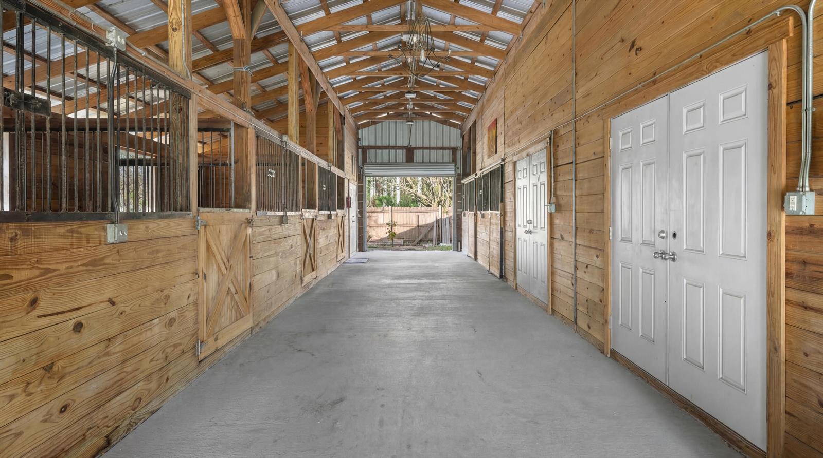 A horse barn aisle with concrete flooring, wooden stalls, and white double doors — 12440 Tangerine Boulevard, FL 33412, FL