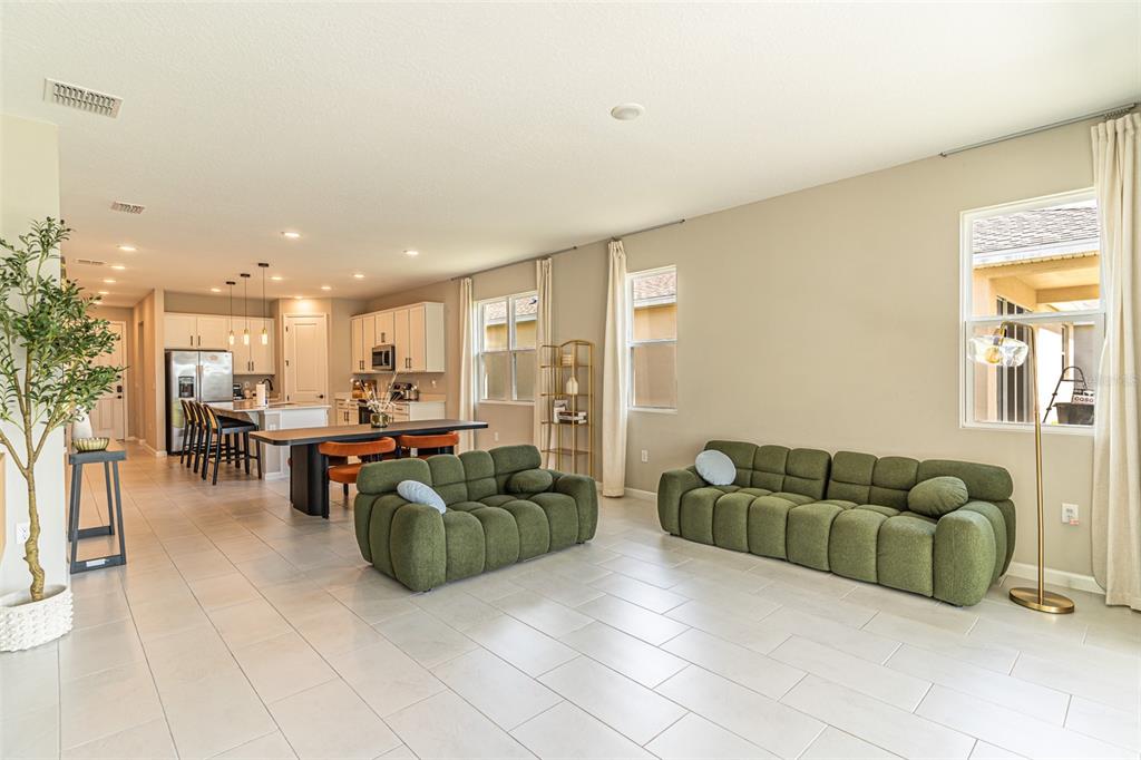 An open-concept living room and kitchen featuring green sofas, tile flooring, and neutral walls — 148 HILLTOP BLOOM LOOP, HAINES CITY, FL